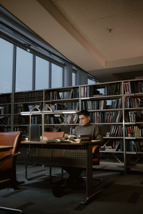 Estudiante investigando en biblioteca con laptop — IA para research académico